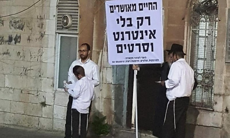 הרב עם השלט ליד בית המדרש של קרלין בירושלים